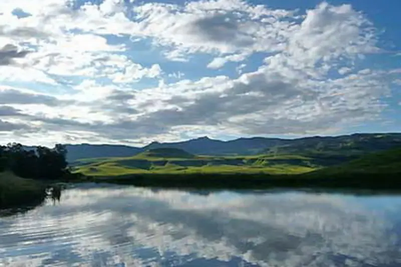 A still dam reflecting clouds, with green hills behind